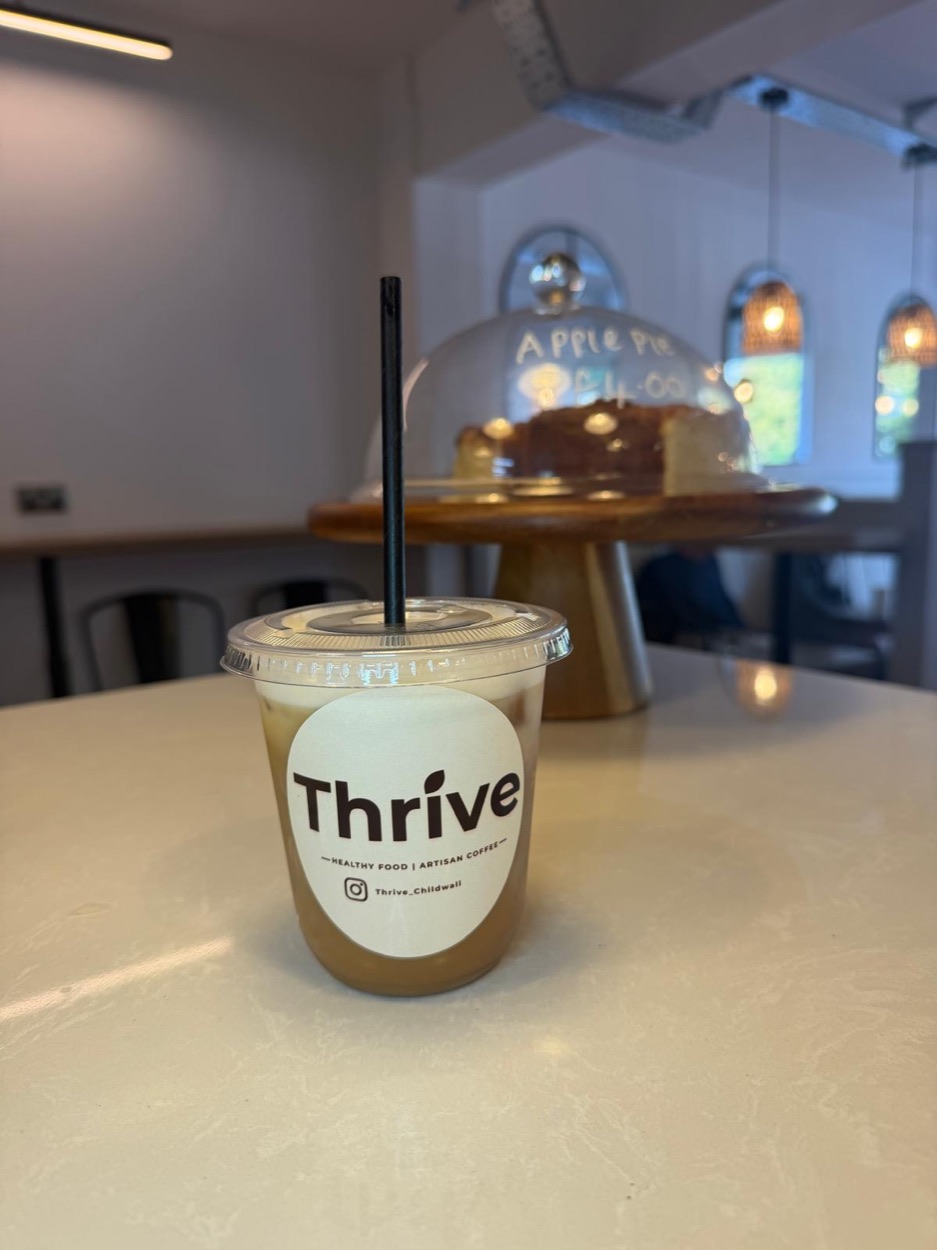 An iced coffee in a Thrive branded cup with apple pie under a glass dome behind